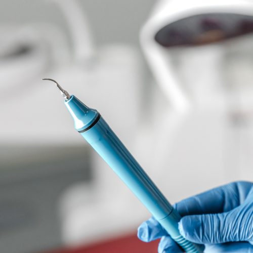Female hand of dentist in blue gloves holding ultrasonic teeth cleaning machine removing calculus and plaque. Oral hygiene and human teeth treatment concept